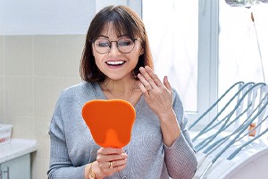 A woman admiring her new dental crown in a hand mirror