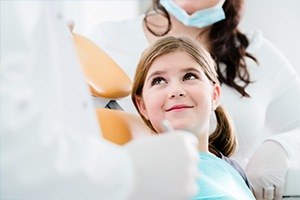 Young girl in dental exam chair looking at dentist