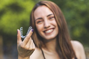 Young woman holding aligner, happy she could afford Invisalign 