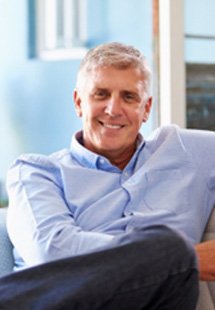 Man with dental implants smiling while sitting on couch