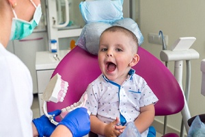A little boy sitting in a dentist’s chair and opening his mouth while a dentist shows him how to brush his teeth