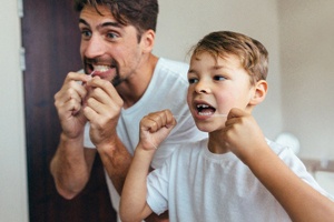 A father and son flossing their teeth while standing in front of a mirror in their bathroom