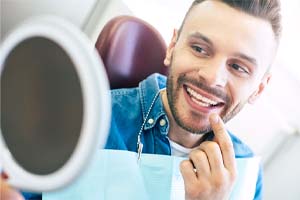 Man examining smile with mirror after seeing Dallas emergency dentist