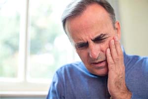 Man with a dental emergency in Dallas holding his cheek