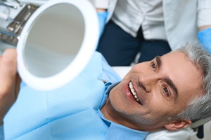 A middle-aged man admiring his new smile in the mirror after receiving dental implants