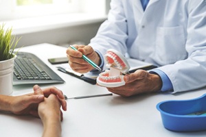 A dentist holding a mouth mold while discussing the cost of dental implants with a patient