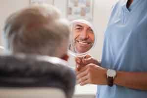 Man smiling while looking at reflection in handheld mirror