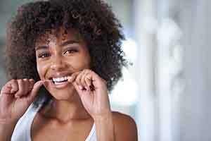 Woman smiling while flossing her teeth in bathroom