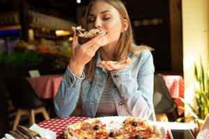 Woman enjoying slice of pizza in restaurant