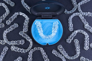 Many Invisalign clear aligners and Invisalign case against dark background