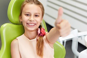 Young girl in dental chair giving thumbs up