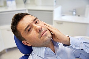 Man in dental chair holding cheek