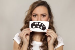 A woman holding a picture of an unhealthy smile over her face.