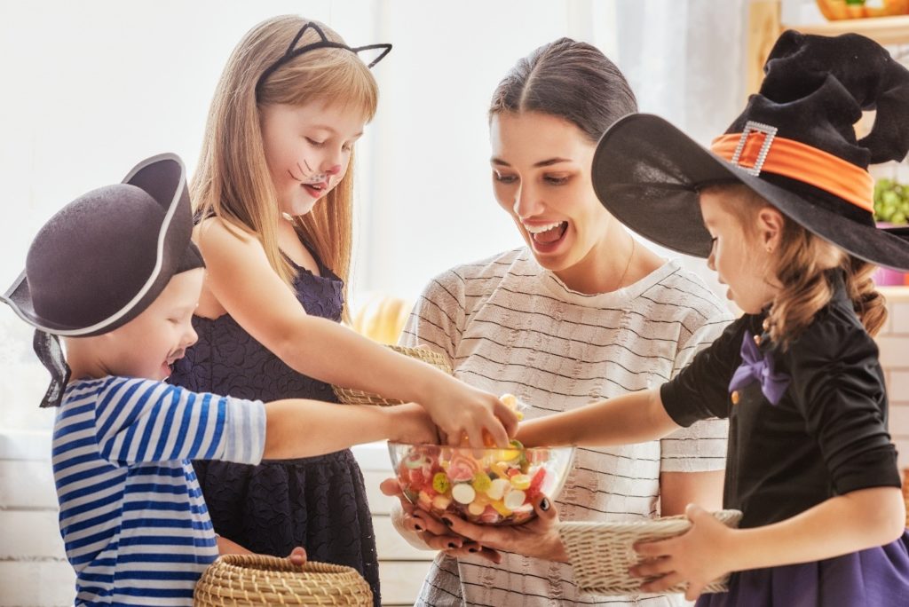 Mom sharing Halloween candy with kids in costumes